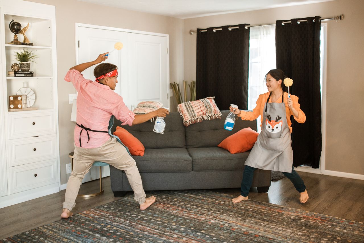 heros-img A joyful couple engages in a playful cleaning fight in their living room, showcasing light-hearted domestic life.